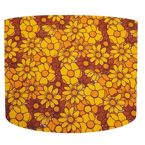 May include: A lampshade with a retro floral design. The pattern features yellow and orange flowers on a brown backdrop. The flowers have a daisy-like shape and are arranged in a repeating pattern.