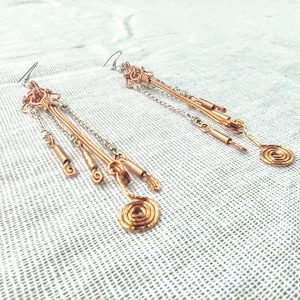 May include: A pair of long, dangling earrings made of copper and silver wire. The earrings feature multiple strands of wire, including a spiral at the bottom.