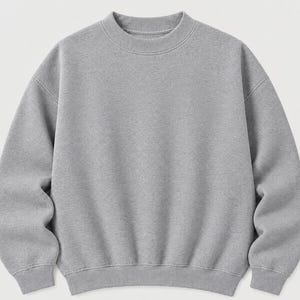 May include: A solid light gray crewneck sweatshirt featuring long sleeves with dropped shoulders, a ribbed collar, and ribbed cuffs at the wrists and hem. The garment is constructed from a soft, fleeced fabric with a consistent heathered texture.