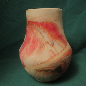 May include: A handmade ceramic vase with a unique, swirled design. The vase features a light beige top and a body with vibrant red, orange, and cream-colored patterns. The vase has a rounded base and a slightly flared opening, showcasing a blend of natural and artistic elements.