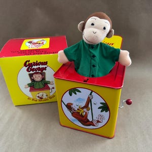 Puszka z 1995 r. z serii Curious George-Schylling Classic Series „Jack-In-Box” – przekręć uchwyt... Usłysz muzykę... Wyskakuje George!