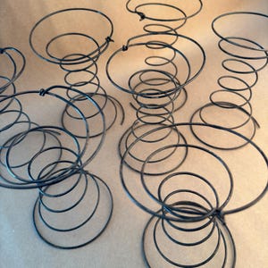 May include: A set of six vintage metal bed spring coils. The coils are black and have a rusty patina. They are arranged in a circular pattern on a brown surface.