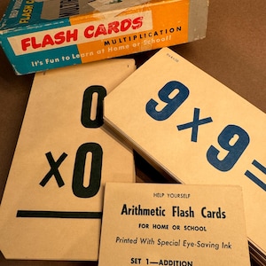 May include: A set of brown flash cards for learning multiplication. The cards have blue and black numbers and symbols. The box for the cards is yellow and blue and says "Flash Cards Multiplication It's Fun to Learn at Home or School!"