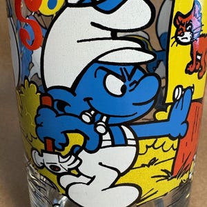 Könnte beinhalten: Ein klares Glas mit einer Cartoon-Illustration von Handwerker Schlumpf. Der Schlumpf ist blau mit weißer Mütze und Hose und hält einen Schraubenschlüssel. Auf dem Glas steht "Handy Smurf".