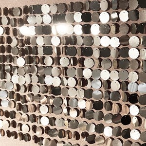 May include: A wall covered in silver and gold round sequins. The sequins are arranged in a staggered pattern, creating a shimmering and reflective surface.