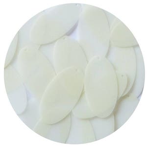 Pode incluir: Uma coleção de lantejoulas ovais de cor branco-quebrado. As lantejoulas estão espalhadas sobre um fundo branco.