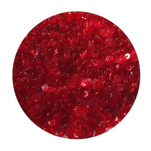 May include: A close-up image of a pile of red sequins. The sequins are small and round, and they are arranged in a random pattern.