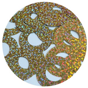 May include: A close-up of a pile of gold iridescent sequins with a hole in the center. The sequins are arranged in a circular pattern.