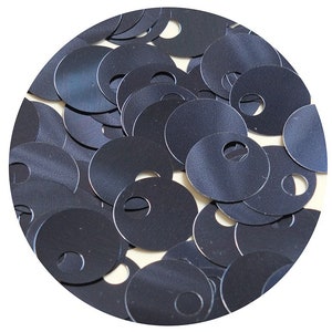 May include: A close-up of a pile of black sequins with a hole in the center of each sequin.