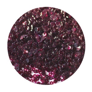 May include: A close-up of a pile of small, round, iridescent sequins in a deep burgundy color.