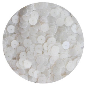 May include: A close-up image of a large quantity of white round sequins. The sequins are scattered randomly and appear to be made of a shiny, iridescent material.
