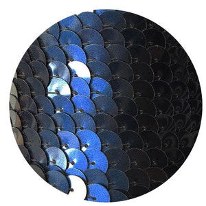 May include: Circular design of overlapping, iridescent blue and black sequins. The sequins create a gradient effect, shifting from bright blue to dark black. The image is set against a plain white background.