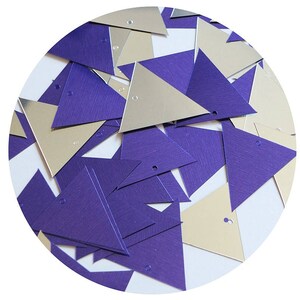 May include: A pile of purple and silver triangle sequins. The sequins are scattered on a white background.