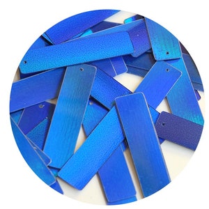 May include: A pile of iridescent blue rectangular sequins with a hole in the center of each sequin.