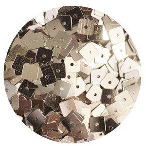 May include: A close-up of a pile of silver square sequins with a hole in the centre of each sequin.