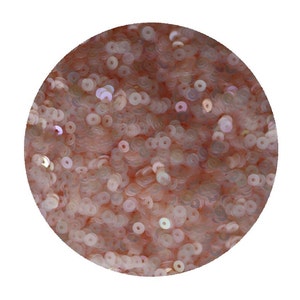 May include: A close-up of a pile of iridescent pink sequins. The sequins are small and round, with a hole in the center. They are arranged in a random pattern.