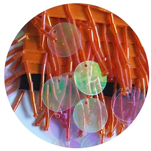 Pode incluir: Franja laranja com lantejoulas redondas iridescentes. A franja é feita de pequenas contas laranja finas.