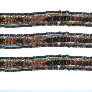 May include: A close-up of three rows of brown and gold beads with sequins. The beads are arranged in a repeating pattern.