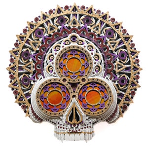 May include: A white, gold, and purple skull with a mandala design on the top. The skull has three orange eyes and a detailed design.