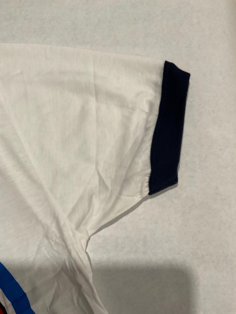 Puede incluir: Camiseta blanca con pu&ntilde;o de manga azul marino. La camiseta tiene un dise&ntilde;o sencillo y parece estar hecha de una tela suave y ligera. El pu&ntilde;o de la manga es de color azul marino liso.