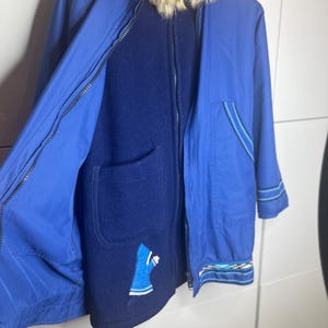 Op de afbeelding: Een blauwe en donkerblauwe omkeerbare jas met een bontkraag. De jas heeft een ritssluiting en een zak aan de binnenkant. De jas heeft een blauw en wit ontwerp aan de onderkant.