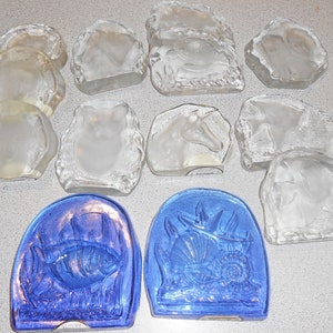 Peut inclure: Une collection de presse-papiers en verre transparent avec différents motifs d'animaux et de la nature. Certains presse-papiers sont empilés les uns sur les autres. Deux presse-papiers sont bleus avec un motif de poisson et de coquillage.