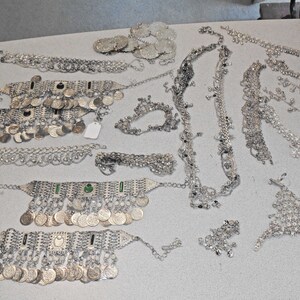 May include: A collection of silver belly dancing jewelry, including a variety of necklaces, bracelets, and anklets. The jewelry is decorated with coins, beads, and other embellishments.
