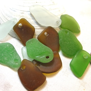 Peut inclure: Une collection de onze morceaux de verre de mer dépolis et lisses dans des tons de vert, brun et blanc transparent. Chaque pièce comporte un petit trou pré-percé pour la création de bijoux. Une pièce canadienne de 25 cents indique l'échelle.