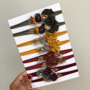 Puede incluir: Conjunto de ocho diademas el&aacute;sticas con diferentes telas de colores y adornos florales. Los colores son verde oliva, mostaza, &oacute;xido y rojo oscuro.