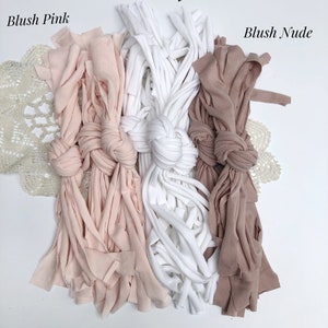May include: Three bundles of fabric yarn in blush pink, ivory, and blush nude colors. The yarn is arranged in a row with a knot in the center of each bundle.
