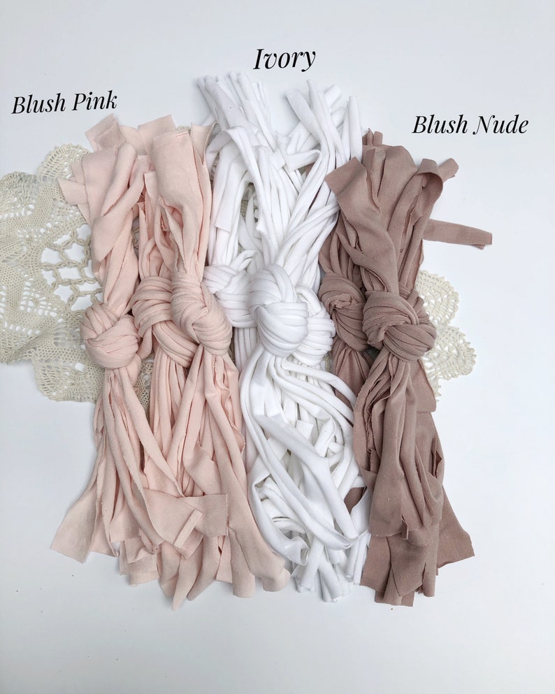 May include: Three bundles of fabric yarn in blush pink, ivory, and blush nude colors. The yarn is arranged in a row with a knot in the center of each bundle.