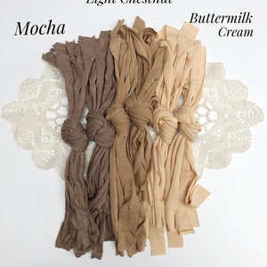 May include: Three bundles of fabric in shades of brown, light chestnut, and buttermilk cream. The fabric is tied in knots and arranged in a row on a white surface.