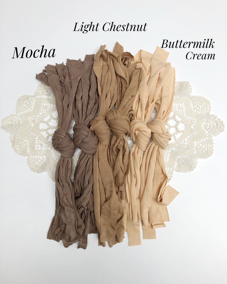 May include: Three bundles of fabric in shades of brown, light chestnut, and buttermilk cream. The fabric is tied in knots and arranged in a row on a white surface.
