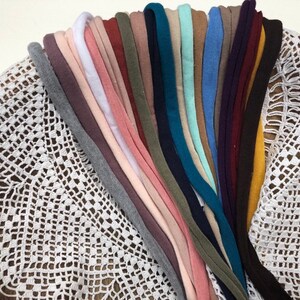 Puede incluir: Una colecci&oacute;n de 20 diademas de tela de diferentes colores, dispuestas en forma de abanico sobre una superficie de crochet blanco.