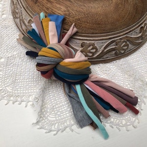 Puede incluir: Un manojo de recortes de tela de colores atados en un nudo. La tela es una mezcla de texturas y colores, incluyendo rosa, azul, verde, amarillo y marr&oacute;n.