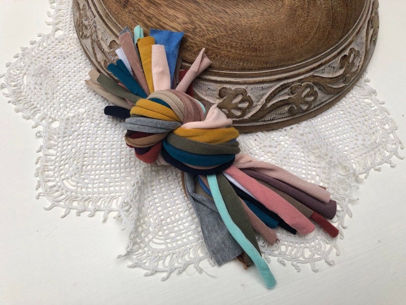 Puede incluir: Un manojo de recortes de tela de colores atados en un nudo. La tela es una mezcla de texturas y colores, incluyendo rosa, azul, verde, amarillo y marr&oacute;n.