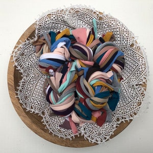 Puede incluir: Un cuenco de madera con un encaje blanco de ganchillo en su interior. El cuenco est&aacute; lleno de una variedad de retazos de tela de colores, incluyendo rosa, azul, verde, amarillo y marr&oacute;n.