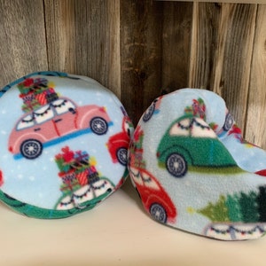 May include: Two blue fleece Christmas-themed car pillows. One is round and the other is shaped like a foot. Both feature a light blue background with red, green, and white cars with Christmas trees and presents on top.