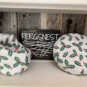 May include: Two white beanbag chairs with a green and red holly pattern. The chairs are on a shelf with a wooden background. A sign above the chairs reads "Fergsnest".