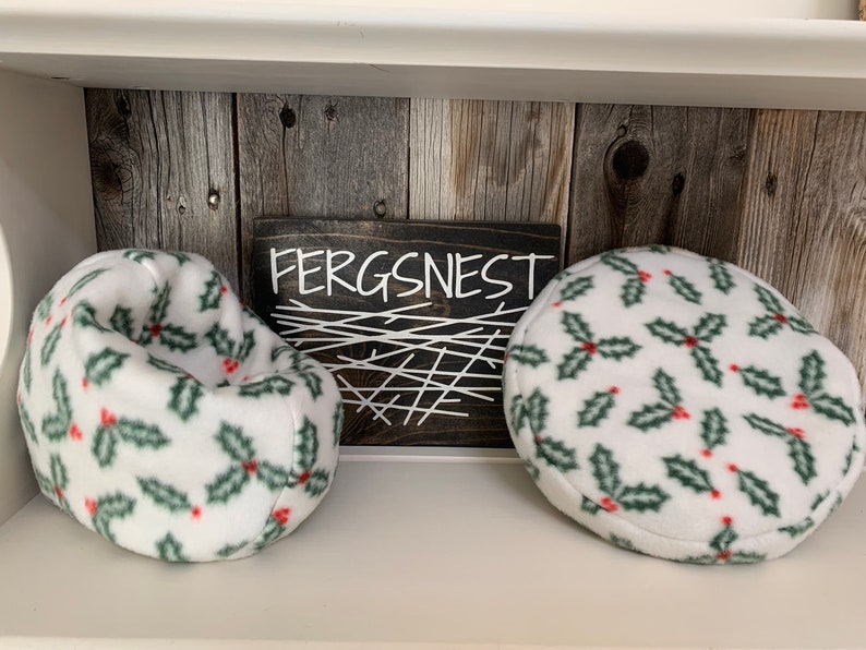 May include: Two white beanbag chairs with a green and red holly pattern. The chairs are on a shelf with a wooden background. A sign above the chairs reads "Fergsnest".