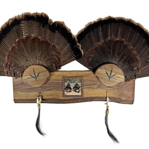 May include: A wooden wall mount with two turkey tail fans, a small picture frame, and two decorative tassels. The mount is made of dark wood with a natural edge.
