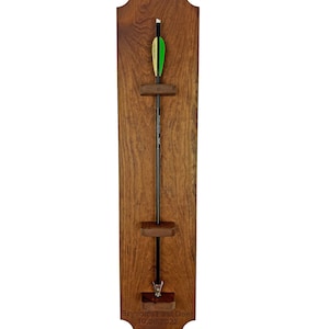 May include: A wooden plaque with a green and yellow arrow mounted on it. The plaque has the text "Bryson's First Deer 10.06.2022" engraved on it.