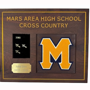 May include: A wooden plaque with the text "MARS AREA HIGH SCHOOL CROSS COUNTRY" in gold lettering. It features a gold and navy blue "M" logo, a small black area with pins, and a gold nameplate with the name "John Doe" and the years "2022-2026".