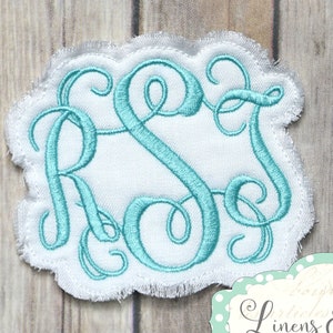 May include: A white monogram patch with a scalloped edge, featuring the embroidered letters R, S, and J in a teal script font. The patch is set against a light wood grain background. A small label with the text "Linens & Lace" is in the bottom right corner.