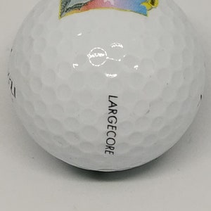 May include: White golf ball with a colorful graphic on one side and the word "LARGE CORE" printed on the other side.
