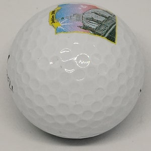 May include: White golf ball with a colorful sticker featuring a building and the text "Jubilee 2001".