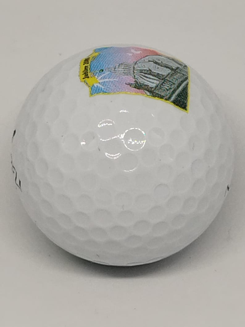 May include: White golf ball with a colorful sticker featuring a building and the text "Jubilee 2001".
