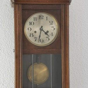 May include: A vintage wooden wall clock with a white face and black hands. The clock has a glass front and a pendulum.