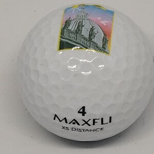 May include: White golf ball with a black and white image of a building with a dome on top. The ball has the number 4 and the text "MAXFLI XS DISTANCE" printed on it.