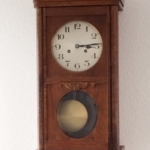 Puede incluir: Un reloj de pared vintage de madera con una esfera blanca y agujas negras. El reloj tiene números romanos y una pequeña ventana en la parte inferior.